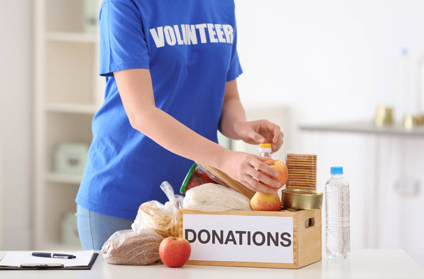 Female volunteer putting food products in donation box indoors - Foto, immagini