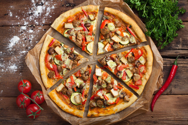 hausgemachte vegane Pizza mit Tomaten, Zucchini, Paprika, Pilzen und Sojafleisch auf einem alten Holztisch. Ansicht von oben - Foto, Bild