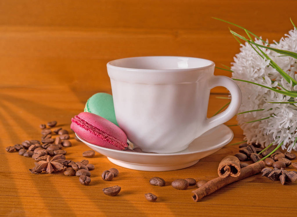 Cup with coffee, cakes on a plate, white flowers, grains of coffee and cinnamon on a wooden background - Valokuva, kuva