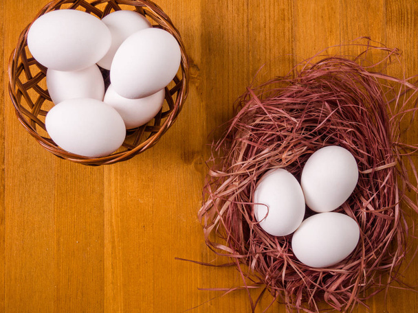 Basket with eggs and a nest with eggs on a wooden background - 写真・画像