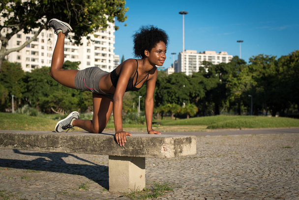 Young Attractive Fitness Woman Doing Knee Raise Crunch Exercise in the City Park on the Concrete Bench - 写真・画像