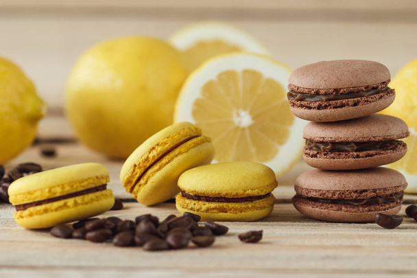 Yellow and brown french macarons with lemons and coffee beans on the wooden board - Fotografie, Obrázek