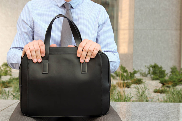 Бізнесмен сидить / відпочиває після робочого дня і тримає шкіряний портфель в руці
 - Фото, зображення