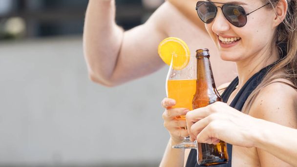 水泳の摩耗でサングラスをかけた女性はカクテルのオレンジ ジュースのガラスを保持します。 - 写真・画像