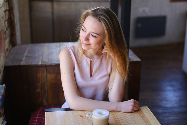 junge Frau sitzt mit Tasse Kaffee am Tisch und posiert für Foto. - Foto, Bild