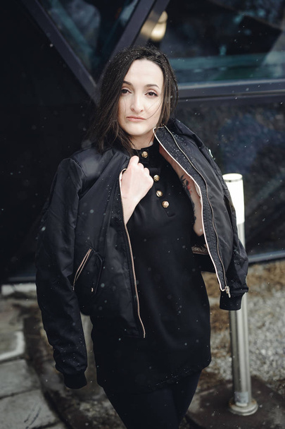 Street Portrait of a woman. fashionable brunette in black clothes on style, a walker  open air in seasons. snowfall snowflakes in frame - Fotoğraf, Görsel