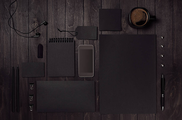 Black blank stationery set with phone, earphone, coffee on dark wood background. Mock up for branding, presentations, design and business portfolios. - Φωτογραφία, εικόνα