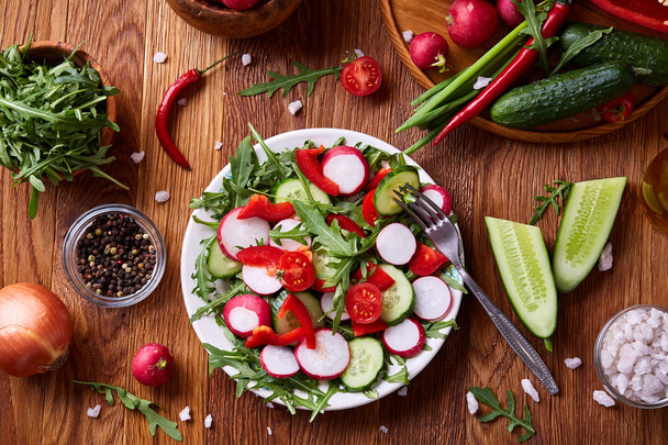 Creative fresh vegetable salad with ruccola, cucumber, tomatoes and raddish on white plate, selective focus - Fotografie, Obrázek