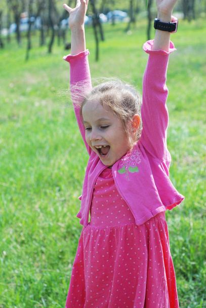 Klein meisje in roze jurk met behulp van slimme horloge roze kleur. Buiten groen Park - Foto, afbeelding