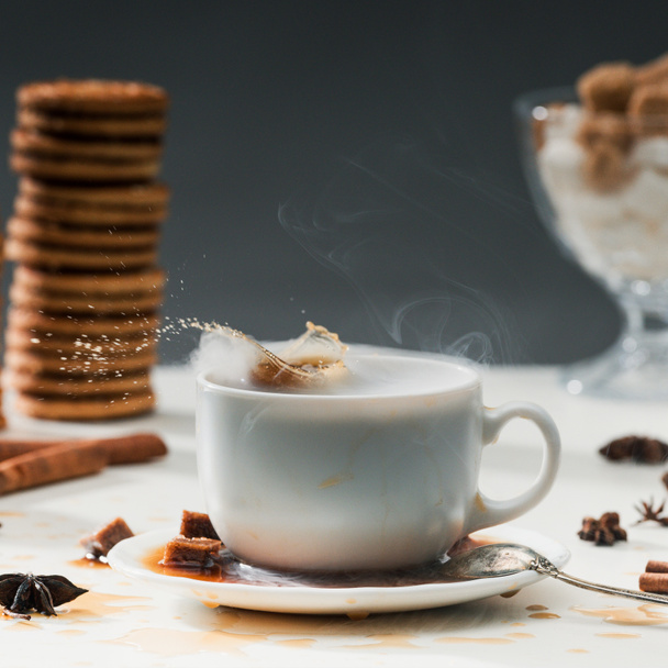 クッキーとスパイスをテーブルの上のコーヒー カップにしぶきブラウン シュガー キューブ - 写真・画像
