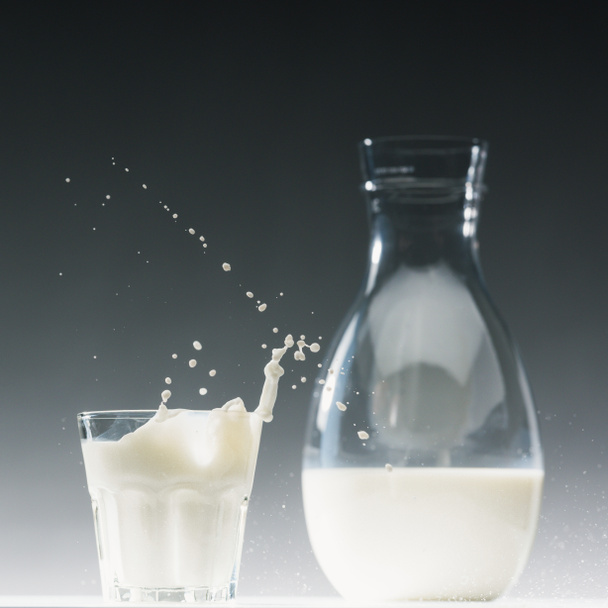 Glass of milk with splashes in front of milk bottle - 写真・画像