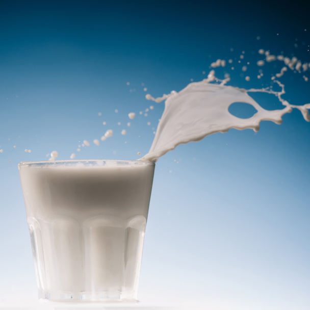 Salpicadura grande sobre un vaso de leche aislado sobre fondo azul
 - Foto, Imagen