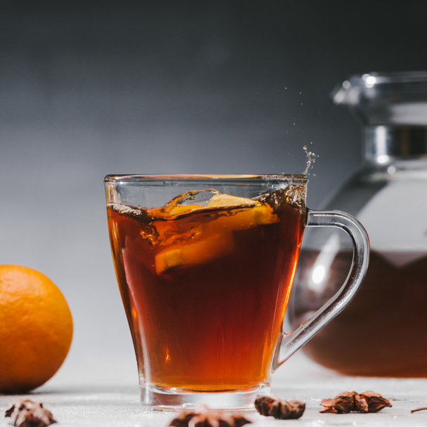Peças de citrinos salpicando na xícara com chá picante preto
 - Foto, Imagem