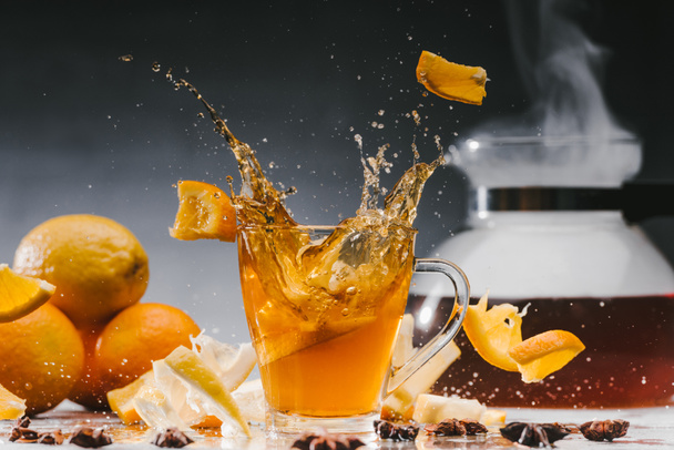 Large splashes of tea in glass cup with citruses and spices - Photo, Image