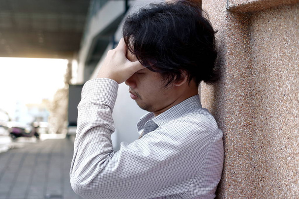 Deprimido y estresado hombre de negocios asiático con las manos en la frente apoyada en la pared
 - Foto, Imagen