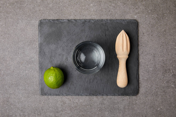 flat lay with wooden squeezer, fresh lime and empty glass on grey surface - Foto, Bild
