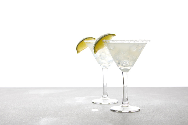 close up view of alcohol margarita cocktails with lime on grey surface on white - Fotografie, Obrázek