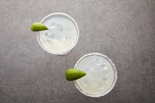 top view of cold alcohol margarita cocktails with pieces of lime on grey tabletop - Foto, Imagem