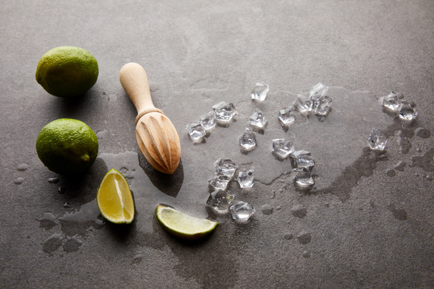 close up view of wooden squeezer, limes and ice cubes for cocktail on grey surface - Фото, зображення