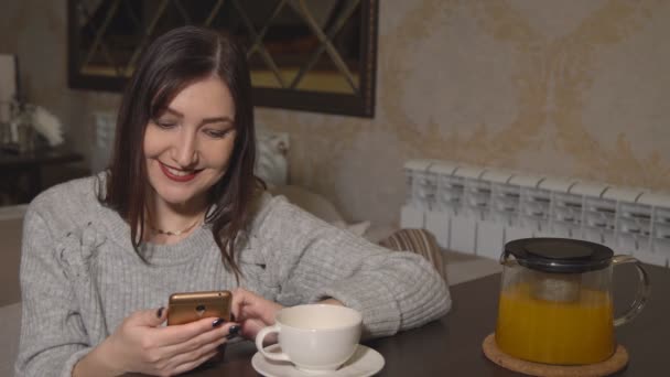 Vrouw in een café aan een tafel drinken thee en bladeren door een band van sociale netwerken - Video