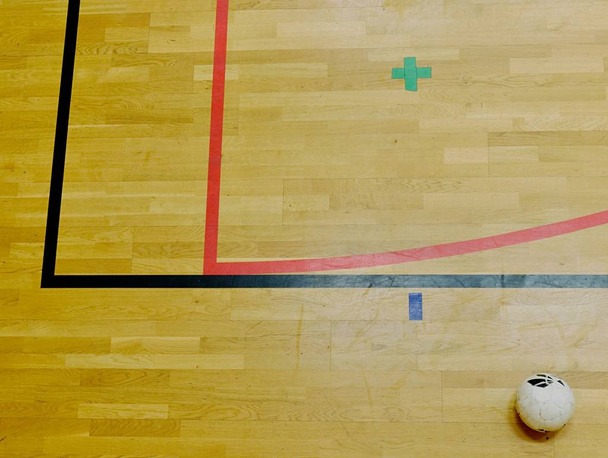 rote und schwarze Linienmarkierungen und Fußballball auf dem Sportboden aus Hartholz. Abgenutzter Fußboden - Foto, Bild