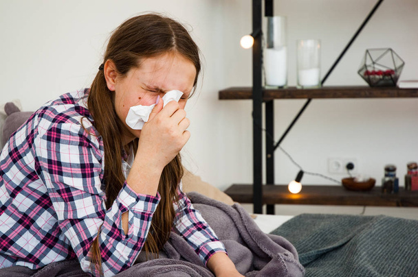 Teini-ikäinen tyttö puhaltaa nenäänsä istuessaan sohvalla. Päänsärky Virusta. Lääkkeet
 - Valokuva, kuva