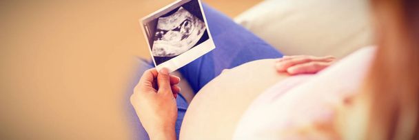 Donna incinta guardando ecografie e toccando la pancia in soggiorno
 - Foto, immagini