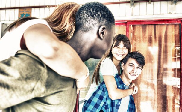 Két multi etnikai párok, boldog tinédzser piggybacking és mosolyog az iskolai folyosón. - Fotó, kép