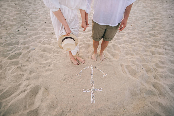 young couple on a sandy shore with an anchor of shells on sand - Fotoğraf, Görsel