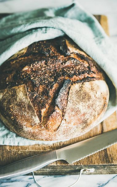 Freshly baked sourdough bread on rustic wooden chopping board over light grey marble background - Фото, зображення