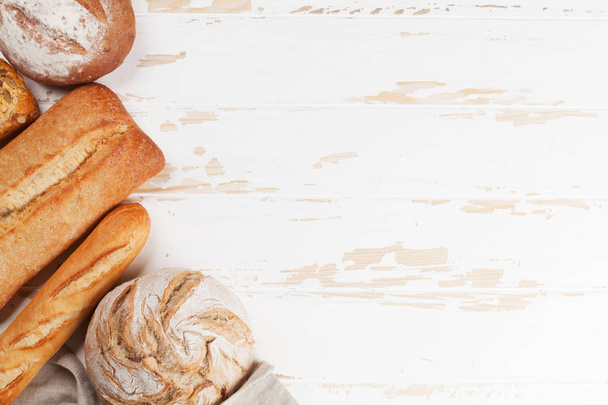 Diverse krokant brood en broodjes op witte houten achtergrond. Bovenaanzicht met ruimte voor uw tekst - Foto, afbeelding
