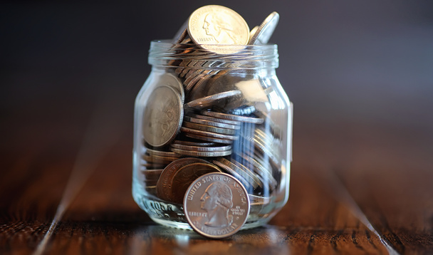 Münzen in einem Glasgefäß auf einem Holzboden. Taschenersparnis durch Münze - Foto, Bild