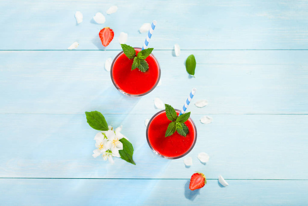 Erdbeer-Smoothie und Blütenblätter auf blauem Hintergrund - Foto, Bild