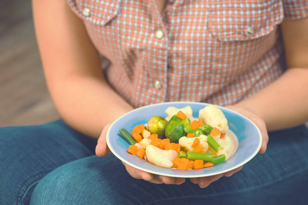 Tyttö pitää lautasella vihanneksia
 - Valokuva, kuva