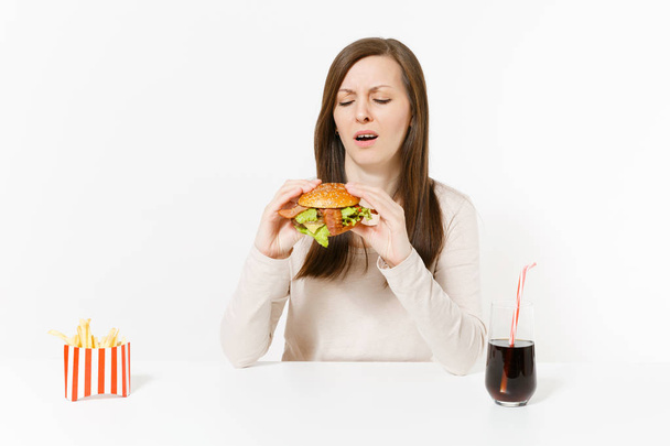 Masada oturan hamburger, patates kızartması, cam şişede cola ile memnun genç kadın beyaz arka plan üzerinde izole. Doğru beslenme veya Amerikan Klasik fast food. Alan kopya alanı ile reklam - Fotoğraf, Görsel
