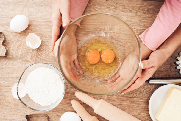 Young grandmother teaching grandchildren breaking eggs in bowl at kitchen - Photo, image