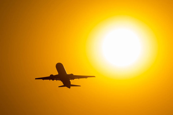 Силуэт самолета, взлетающего во время заката, летит рядом с диском солнца
. - Фото, изображение