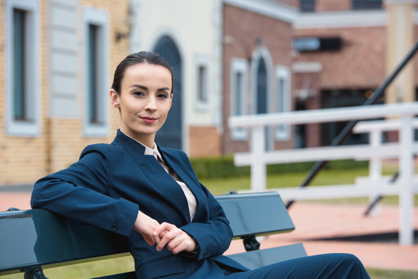 beautiful businesswoman sitting on bench and looking at camera - Фото, изображение
