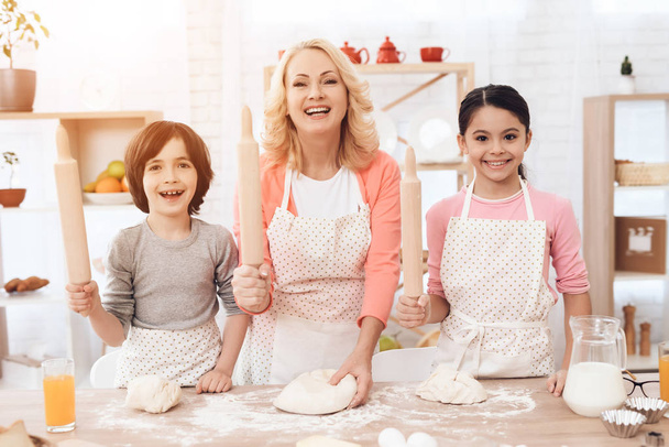 Joven abuela con nietos divirtiéndose mientras preparan galletas en la cocina
 - Foto, imagen