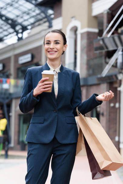 привлекательная деловая женщина стоит с одноразовой чашки кофе и сумки для покупок
 - Фото, изображение