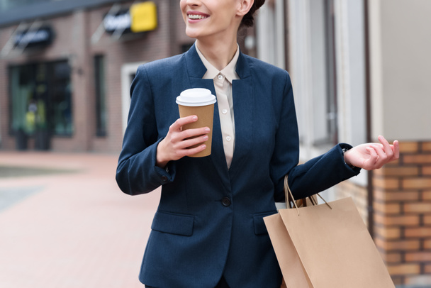 cropped image of businesswoman holding coffee to go and shopping bags - Foto, afbeelding
