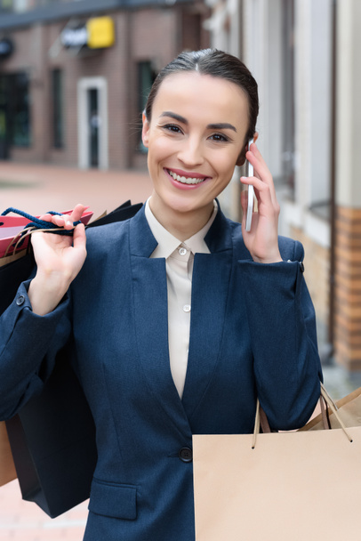 attractive businesswoman talking by smartphone and holding shopping bags - Foto, Imagem