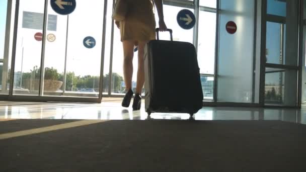 Uma senhora de negócios a sair do aeroporto com a bagagem. Mulher de saltos altos andando com sua mala através de portas de vidro do terminal para o estacionamento de táxi. Viagem ou férias conceito de viagem. Movimento lento
 - Filmagem, Vídeo