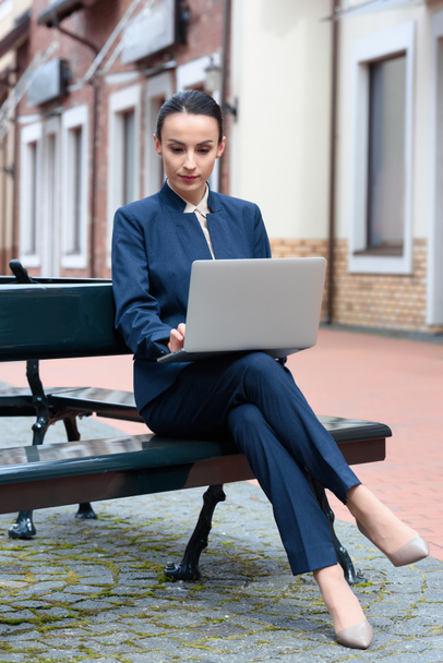 beautiful businesswoman using laptop on bench in city - Foto, Imagem