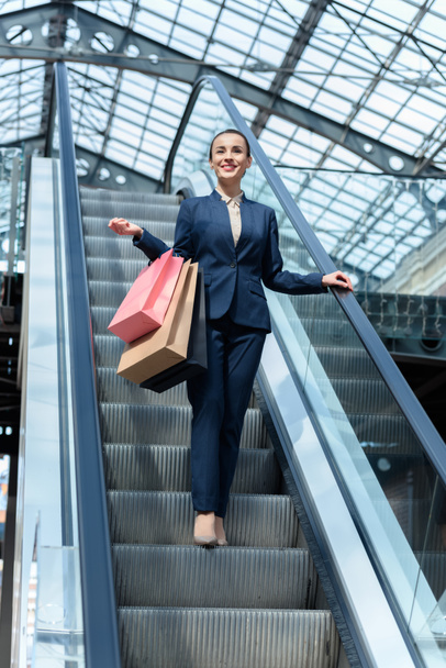 low angle view of attractive businesswoman standing on escalator with shopping bags - Фото, зображення