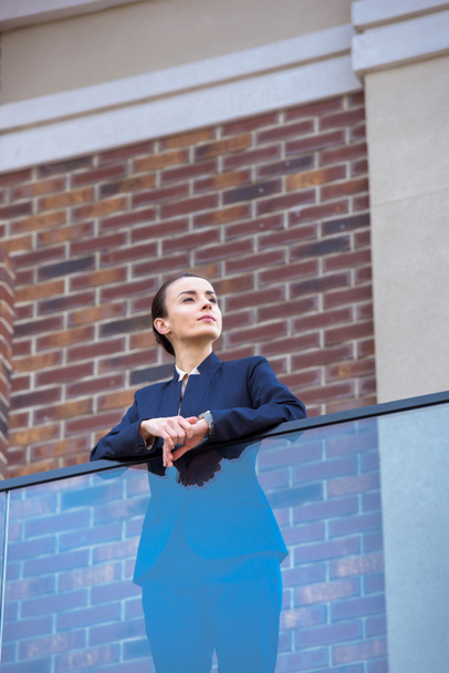 low angle view of beautiful businesswoman standing on balcony and looking away - Foto, Imagen