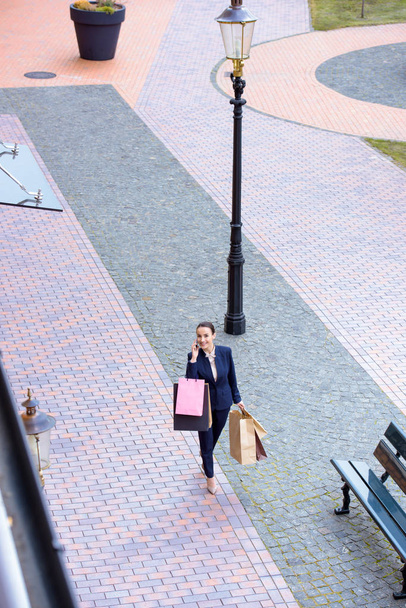 high angle view of attractive businesswoman walking with shopping bags and talking by smartphone - Фото, зображення