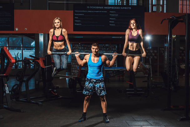Der athletische Mann hebt die Langhantel mit zwei Mädchen als Gewicht und Mädchen, die an der Langhantel hängen. Langhantel mit zwei Mädchen drauf - Foto, Bild
