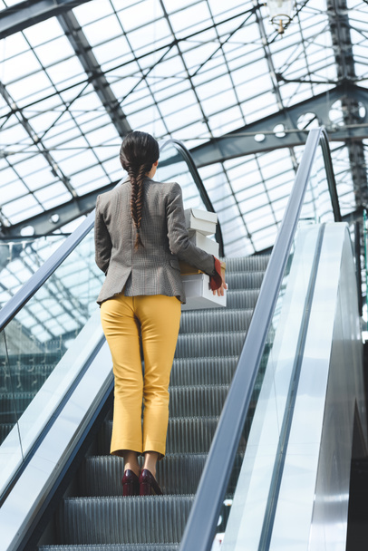 back view of woman standing with shopping boxes on escalator in mall - Photo, Image