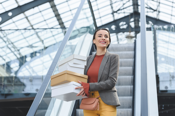 attraktive Frau steht mit Einkaufskartons auf Rolltreppe - Foto, Bild